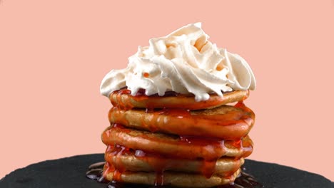 american pancakes with strawberry topping and whipped cream. on a pink background.