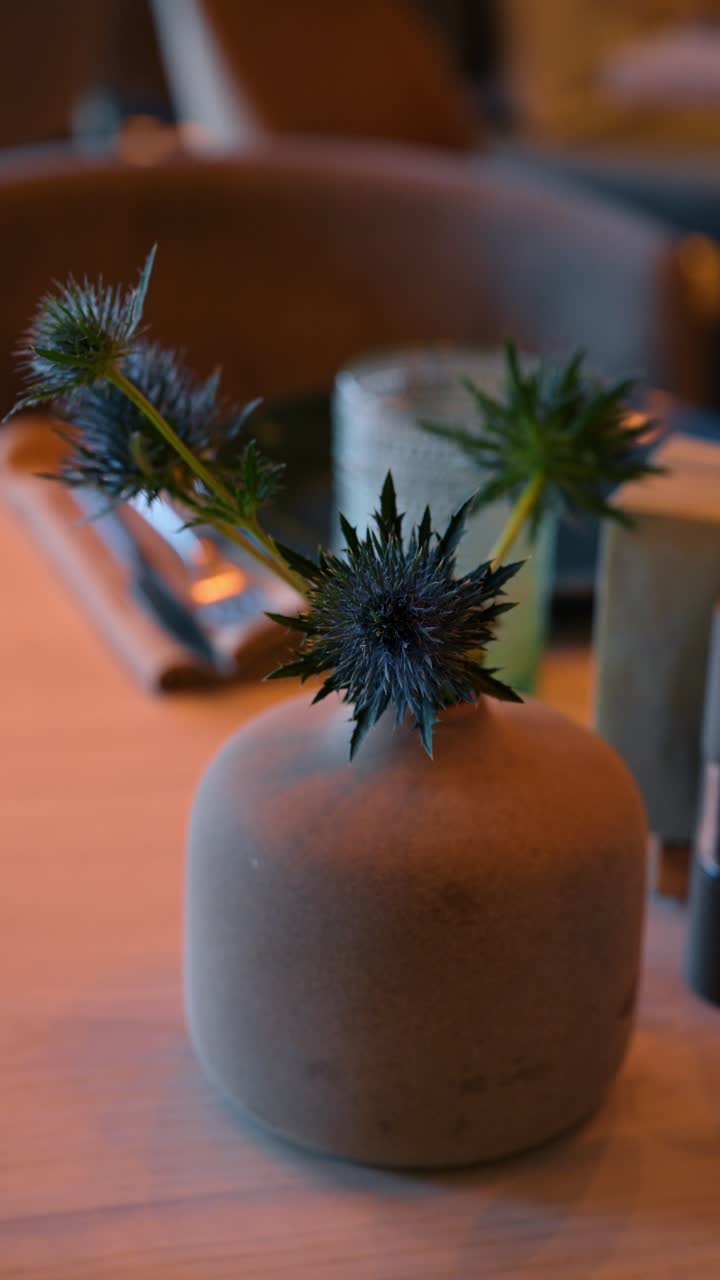 Gros plan d'une fleur de chardon bleu dans un vase en céramique sur une table de restaurant. Mise au point sélective sur la fleur de chardon bleu Eryngium dans un vase rond en argile sur une table en bois avec un arrière-plan flou.