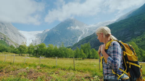 an active woman with a backpack walks against the backdrop of the mountains and the briksdal glacier