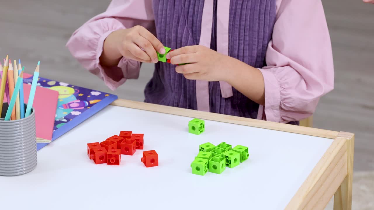 Young student counts and connects red and green math cubes on a bright classroom table