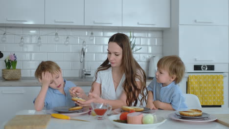 Junge-Mutter-Mit-Zwei-Kleinen-Söhnen-In-Der-Küche-Am-Tisch-Und-Bereitet-Burger-Zum-Mittagessen-Zu