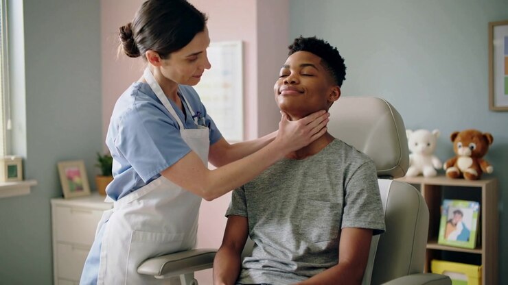 Lifting chin clinician in scrubs, apron palpating teen neck during checkup in pediatric exam chair