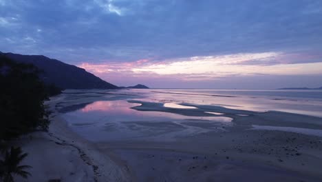 beautiful aerial footage of sunrise over koh phangan in thailand with calm ocean and pink sky colors reflecting on the beach during low tide