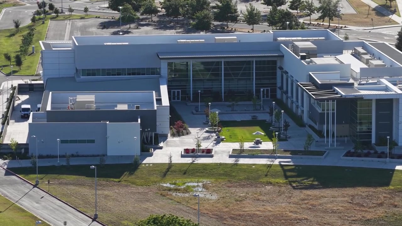 Arquitectura moderna de Clovis Community College en Fresno, California, con edificios contemporáneos, un patio central con césped verde y estacionamientos circundantes, filmado con un dron.