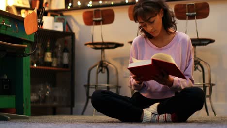 Front-view-of-mixed-race-young-woman-reading-a-book-in-a-comfortable-home-4k