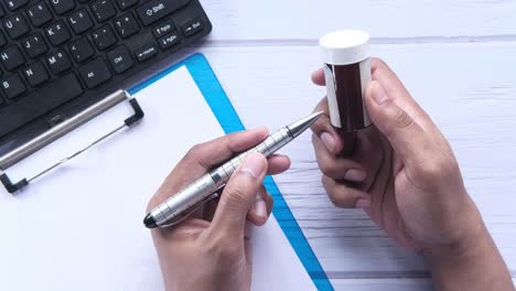 persona que sostiene una botella de pastillas y escribe en un documento