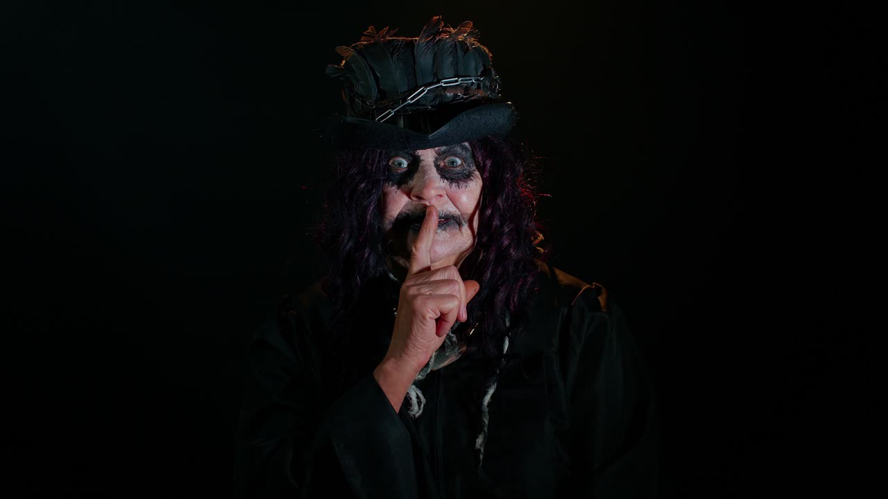 una mujer de edad avanzada espeluznante con maquillaje de bruja de halloween presiona el dedo índice a los labios hace un gesto de silencio
