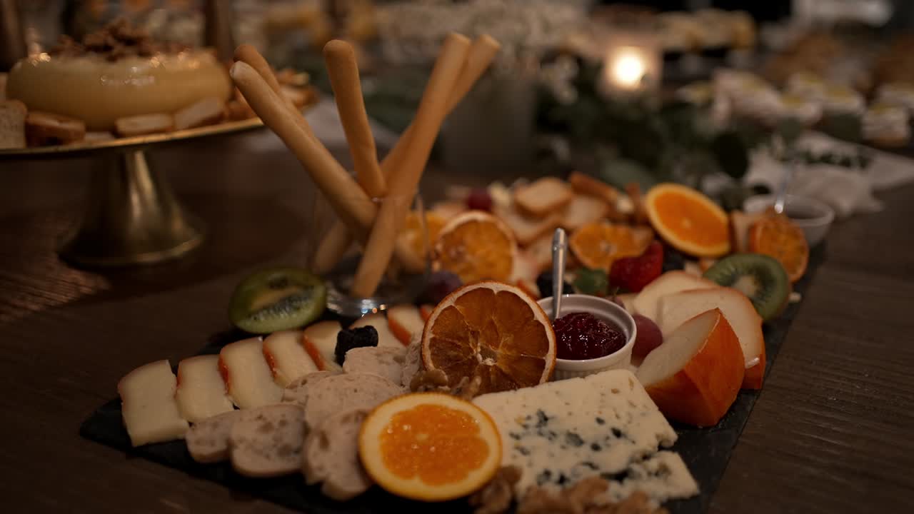 Primer plano de una tabla de quesos con fruta, palitos de pan y mermelada en un evento festivo