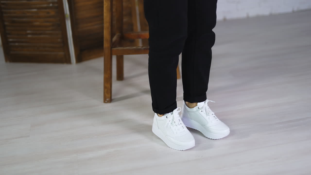 Model jumping in comfortable white sneakers. Woman spinning and hopping to demonstrate fashionable sport footwear.