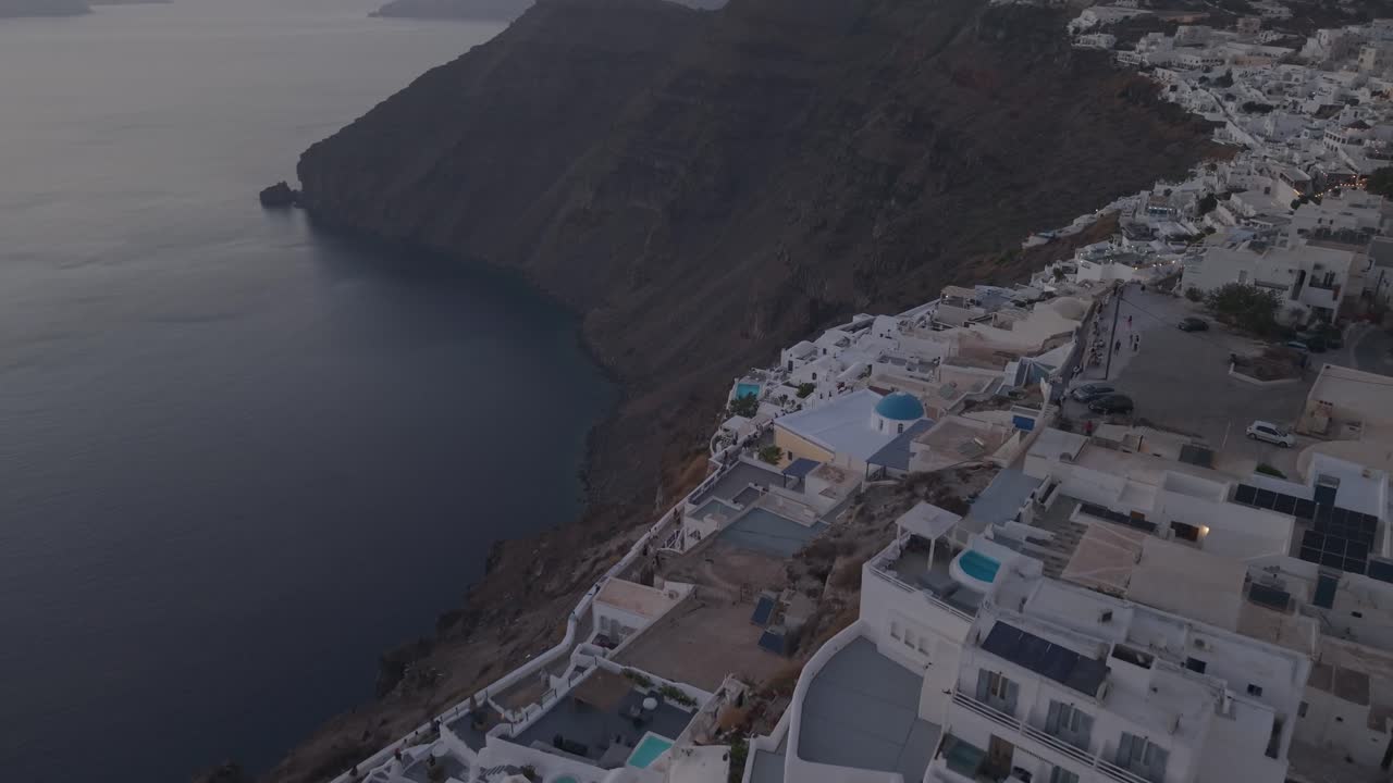En gimbal-tiltning uppåt som börjar från en uppifrån-och-ner-vy av vitkalkade hus i Oia, som långsamt avslöjar den glödande orangea solen när den går ner över Santorinis kaldera