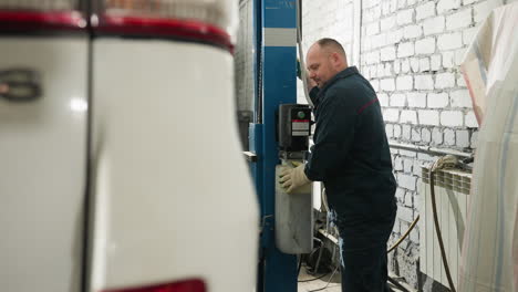 mechanic in blue uniform presses lift button to lower car in garage, with light streaming from background, adding depth and professionalism to the workshop environment