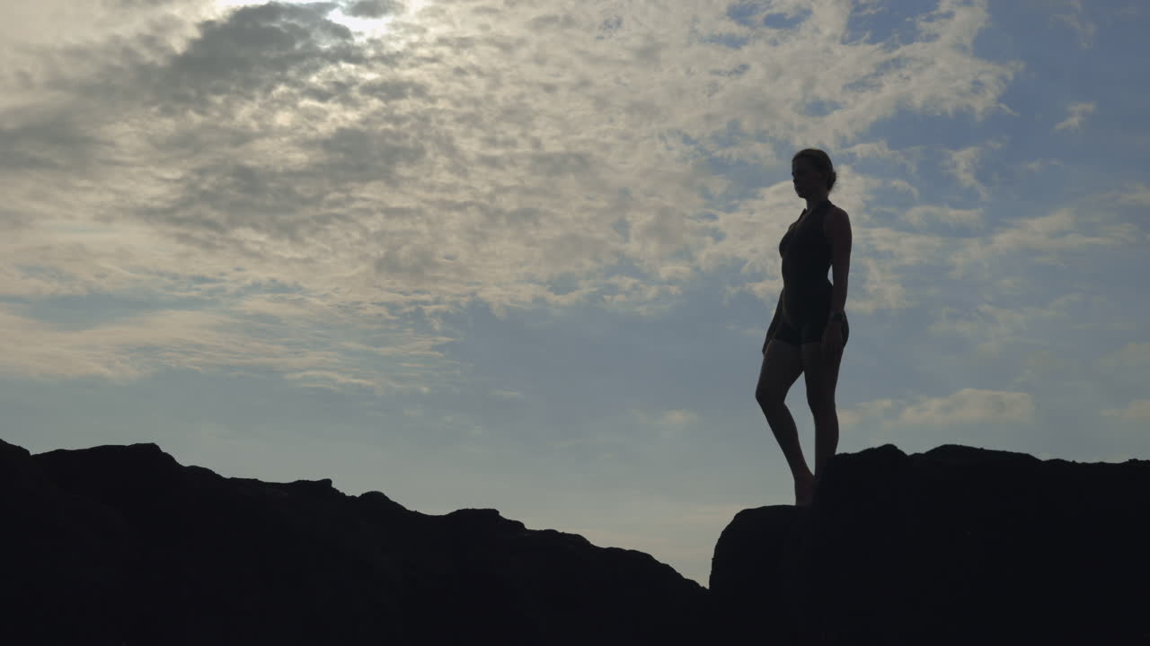 Woman practicing yoga on a rocky outcrop at sunset