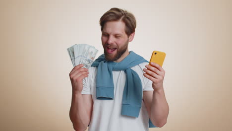 hombre feliz mirando pantalla de teléfono inteligente regocijándose ganar, celebrar, recibir dinero dólar en efectivo premio mayor