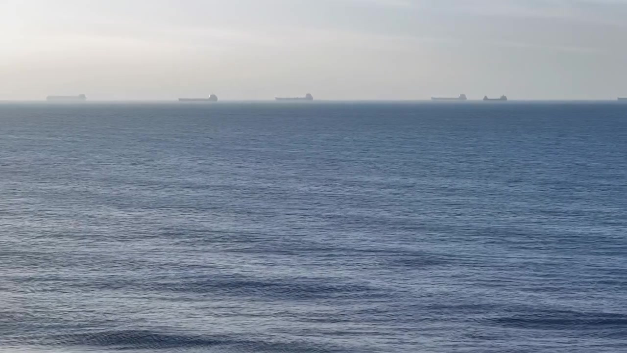et luftfoto af det rolige åbne hav med fjerne skibe og horisonten over vandet, fanget i blå og grå toner, rejse- og ferieindhold med en ren baggrund og rigelig