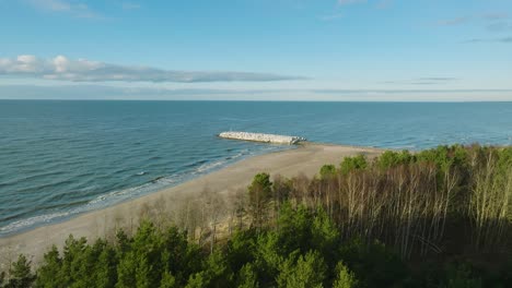 aerial establishing view of protective stone pier with concrete blocks and rocks at baltic sea coastline at liepaja, latvia, strengthening beach against coastal erosion, wide drone shot moving forward