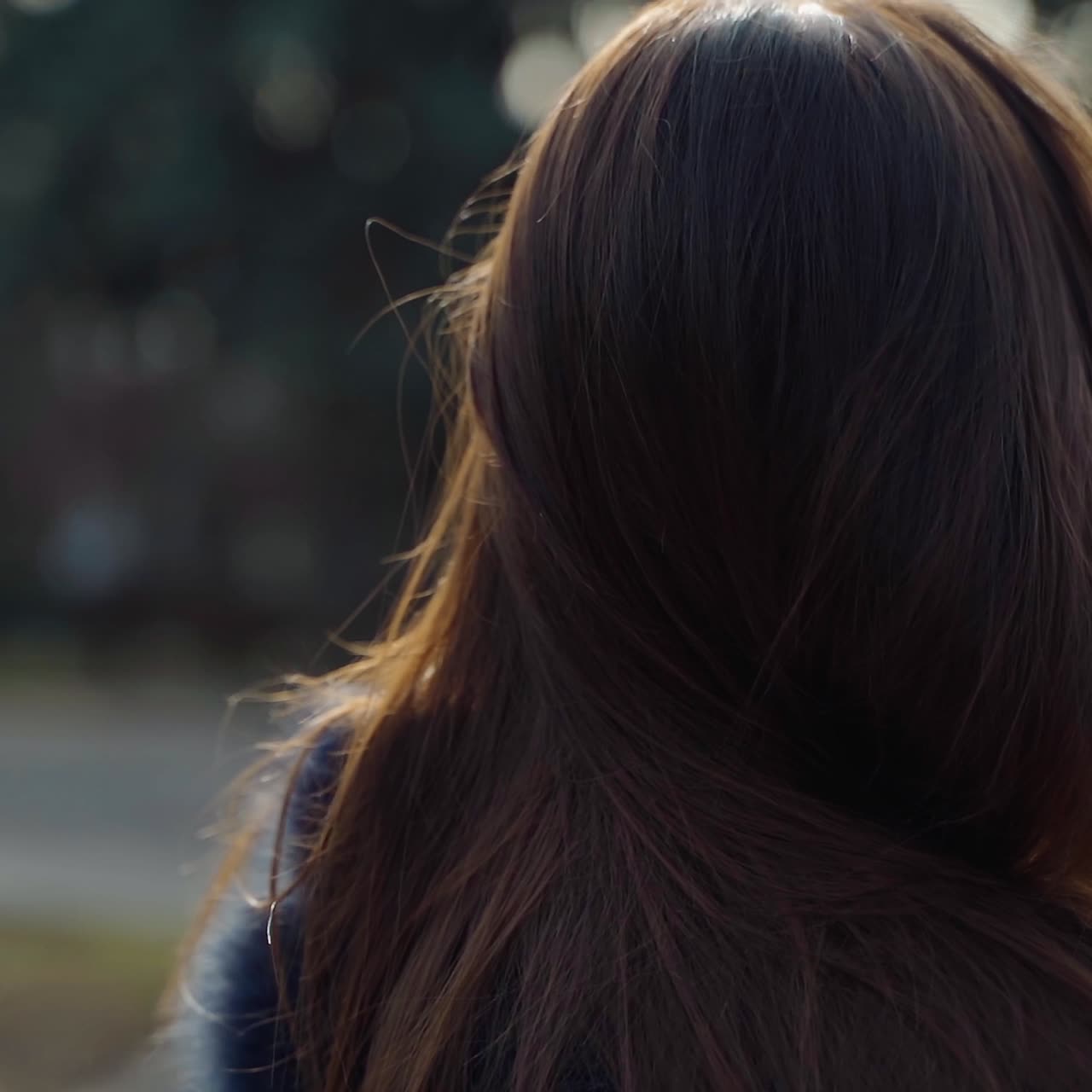 Beautiful brunette in the park. Long-haired girl in fur coat holds plastic cup outdoors. Camera moves round.