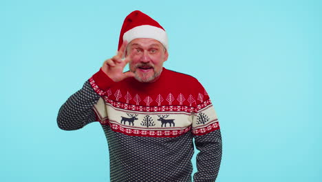 hombre positivo en suéter de navidad con ciervos agita la palma de la mano en el gesto de saludos da la bienvenida a alguien