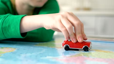 closeup of child hand holding toy red car, world wide travelling on paper map