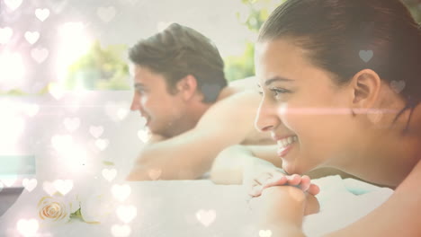 una pareja sonriente relajándose con corazones animados sobre ellos
