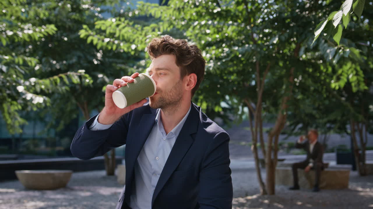 jefe exitoso bebiendo café para llevar sentado solo en el parque soleado de cerca.