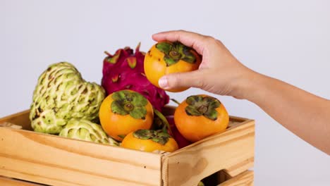 hand interacts with persimmon and fruit crate