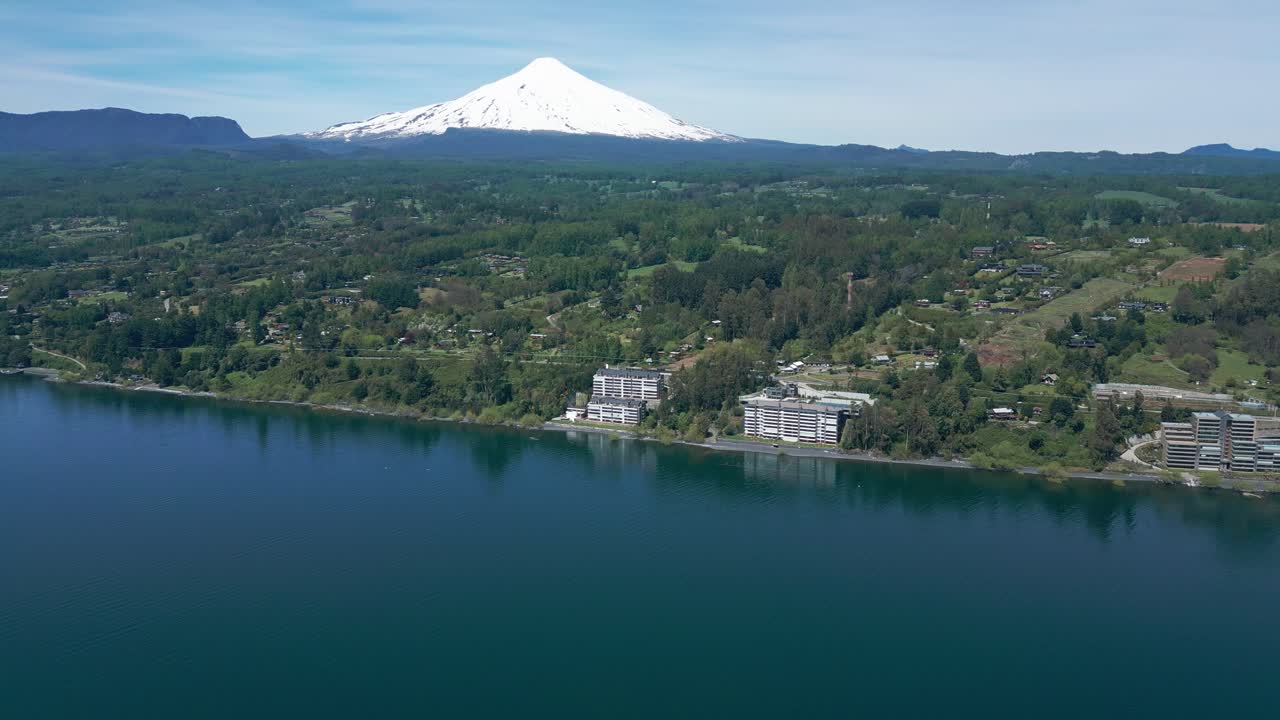 Drone Shot Over Lake and Modern Waterfront Buildings with Snow-Capped Villarrica Volcano in the Background Surrounded by Lush Forest