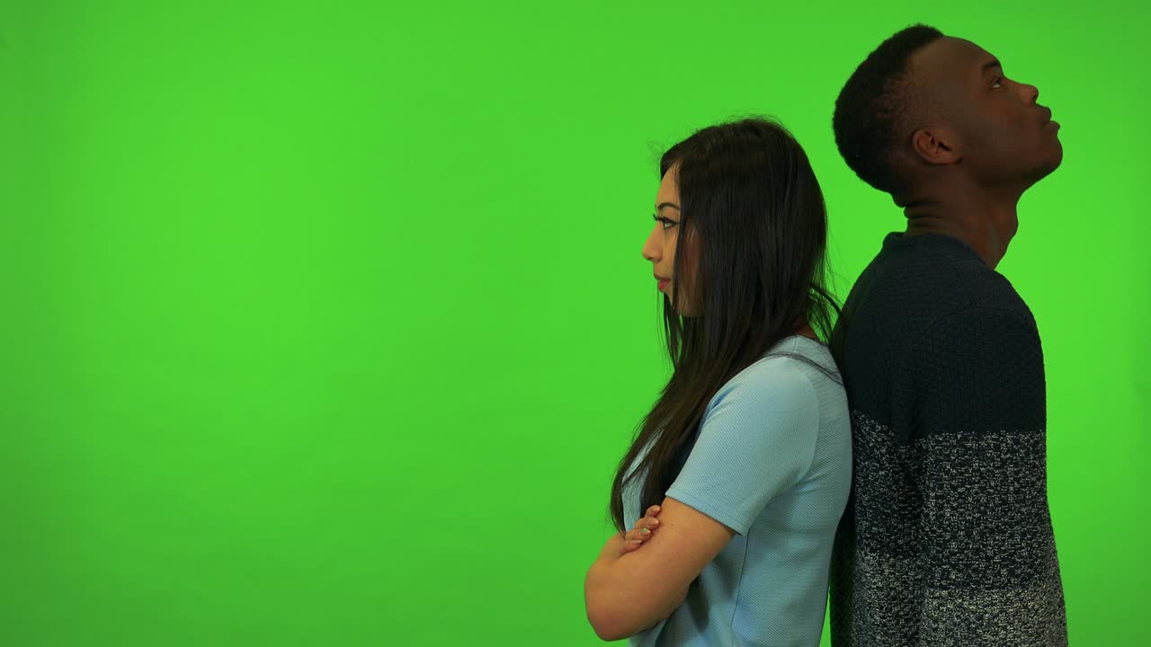 Uma jovem mulher asiática e um jovem homem negro ficam de costas um para o outro, frustrados - estúdio de tela verde