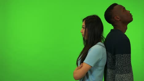 una joven asiática y un joven negro están de espaldas el uno al otro, frustrados - estudio de pantalla verde