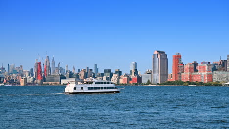 White riverboat goes by the blue waterscape of the Hudson River. New York skyline at backdrop. View from Jersey City