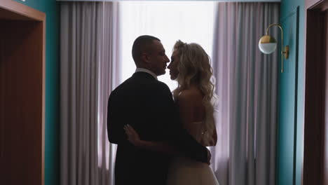 young man kisses nose of blonde curly haired woman by window