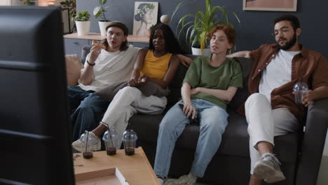 friends watching tv and eating pizza together at home
