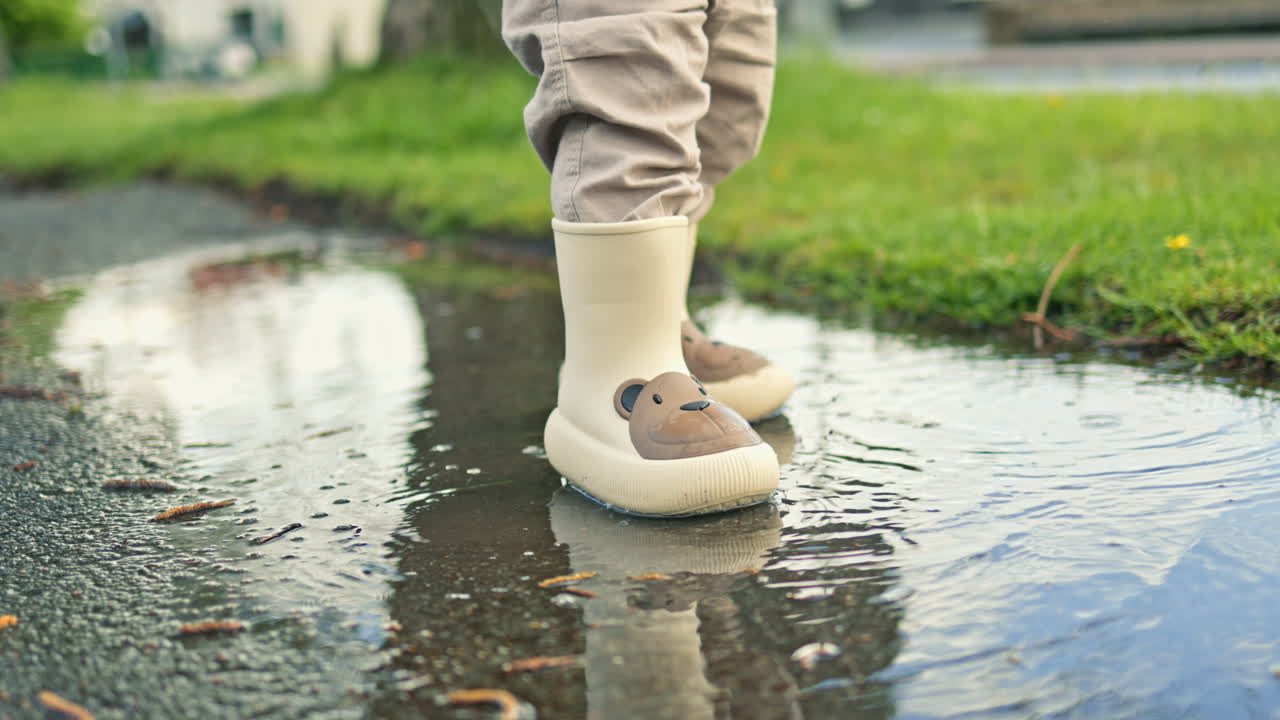 Close-up of Child's Feet in Rain Boots Splashing in Puddle