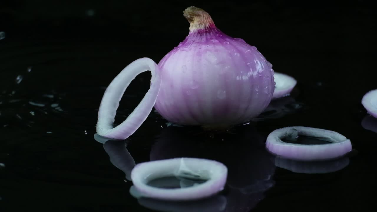 Slow Motion Shot of an Onion and Onion Rings Splashed with a Few Raindrops and a Falling Onion Ring