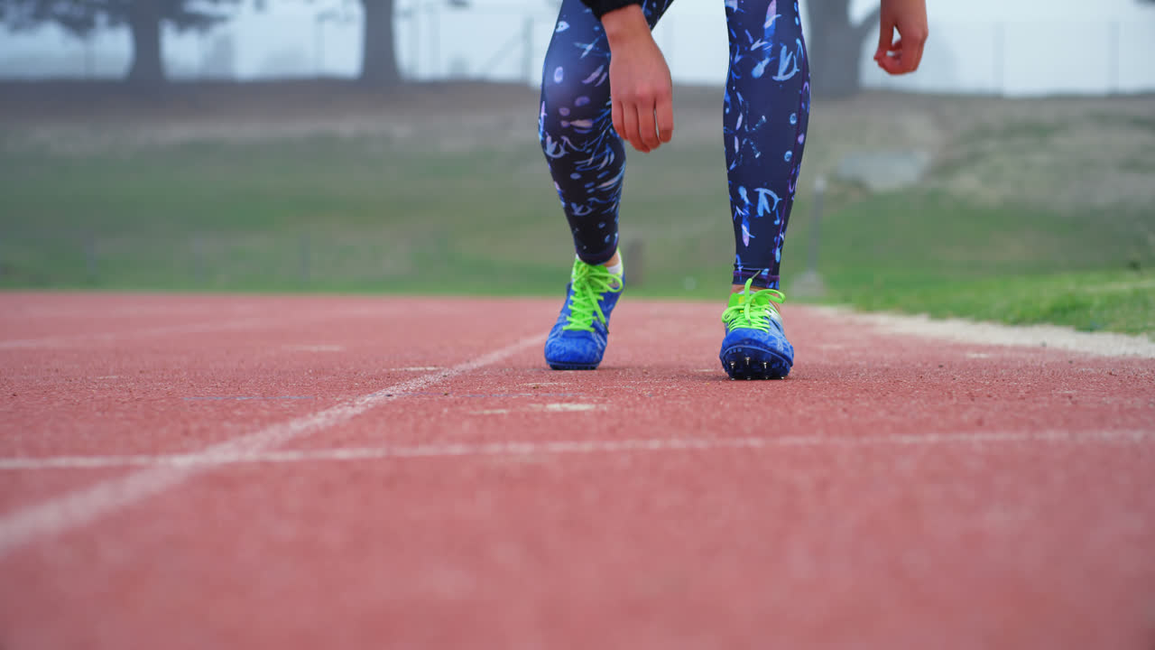 sección baja de atleta femenina atando el cordón de los zapatos en una pista de atletismo en un lugar deportivo 4k