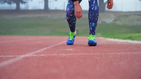 Unterer-Teil-Einer-Sportlerin,-Die-Auf-Einer-Laufstrecke-In-Einer-Sportstätte-Die-Schnürsenkel-Bindet,-4k