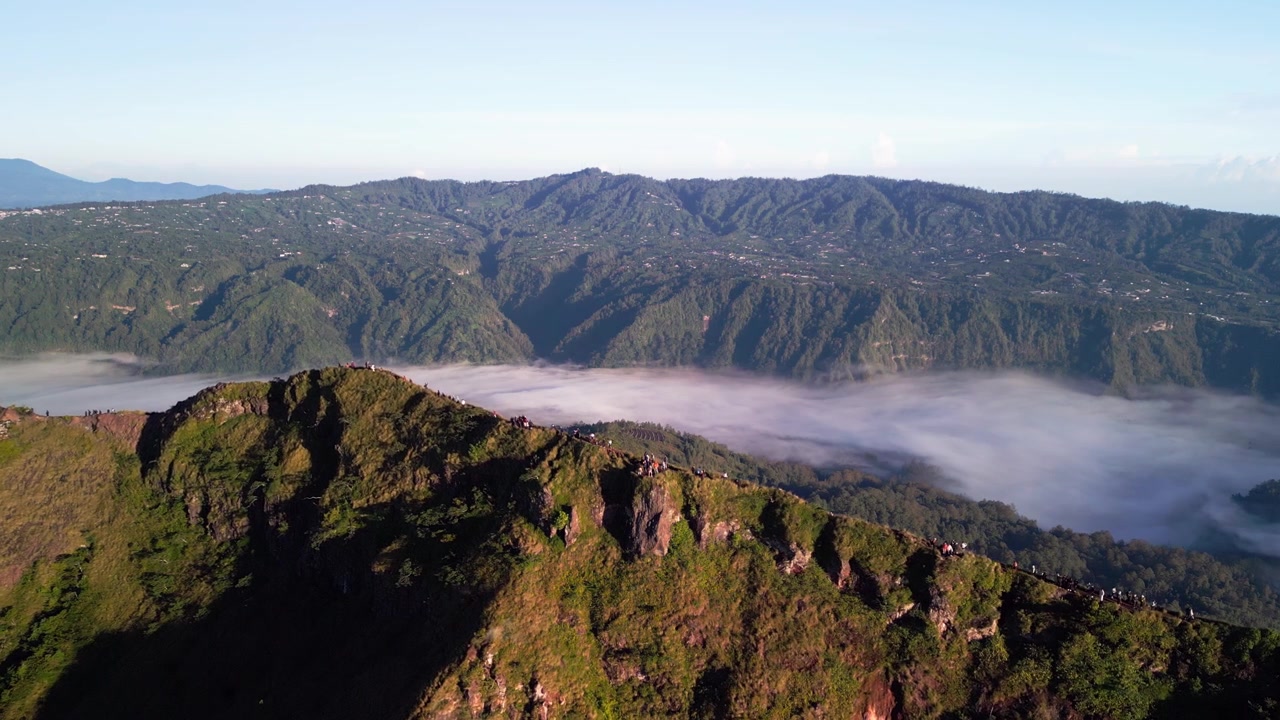 Escursionisti sulla cresta di montagna sul bordo del cratere, persone che si muovono lungo il sentiero sopra un mare di nuvole in pieno giorno soleggiato con pendii ripidi e paesaggio vulcanico d'alta quota, filmato con drone in discesa