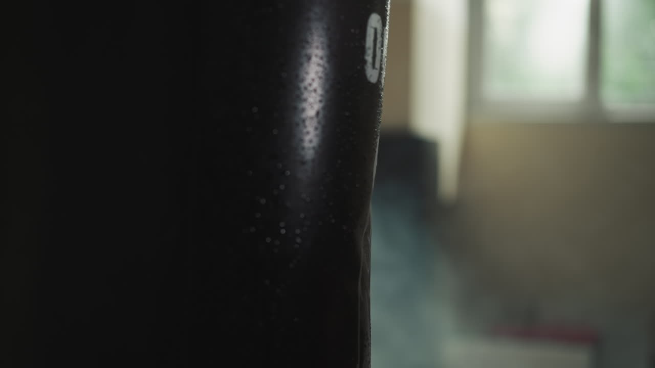 Boxing trainer hand in professional glove hits punching bag with power in gym with equipment. Male expert goes in for sports and gains muscle mass