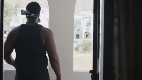 black male walking out of darkness and opening bedroom window and stepping onto balcony to look around in santorini, greece