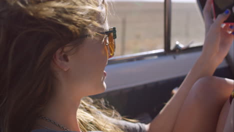 beautiful young woman taking photos with smart phone on road trip in convertible vintage car