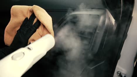 male wearing black gloves cleaning a dashboard side air vent with steam