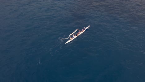 a rowing team paddles a hawaiian outrigger canoe along the ocean in synchrony - aerial bird's eye view