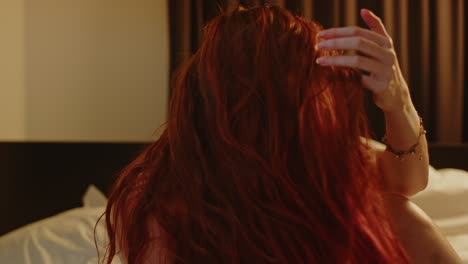 beautiful woman with long red hair sensually sits in bed and looks towards camera