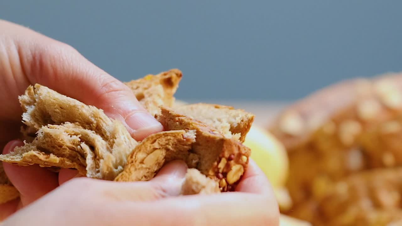 Primo piano di mani che strappano una fetta di pane integrale sopra un tavolo di legno