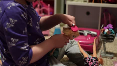 4 year old girl brushing a doll's hair with a tiny pink brush with lots of toys in the background