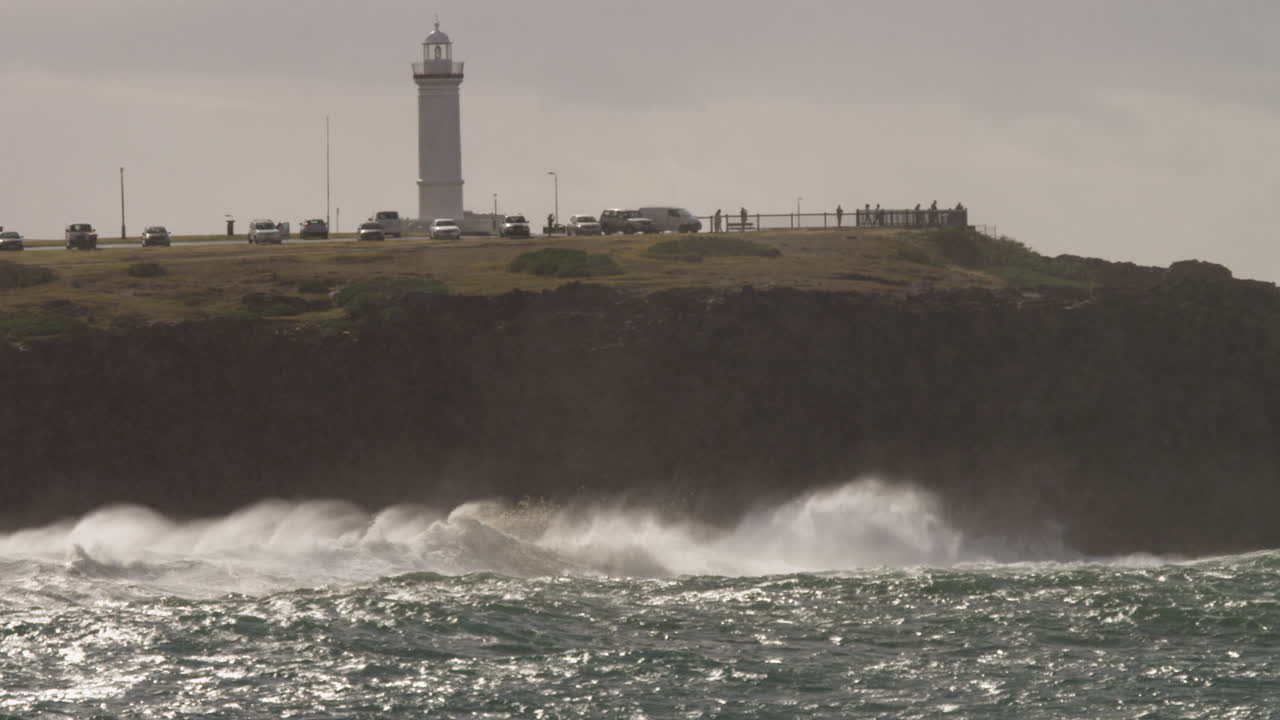 햇살이 내리쬐는 동안 등대 기슭의 바위에 파도가 부서진다