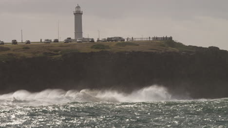 Waves-break-onto-the-rocks-at-the-foot-of-a-lighthouse-during-a-sun-shower