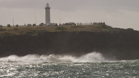 Las-Olas-Rompen-En-Las-Rocas-Al-Pie-De-Un-Faro-Durante-Una-Ducha-De-Sol