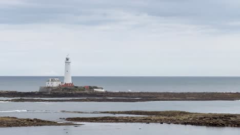 a stationary camera captures a distant lighthouse on a rocky island under cloudy skies, with calm sea and muted daylight, emphasizing tranquil coastal scenery