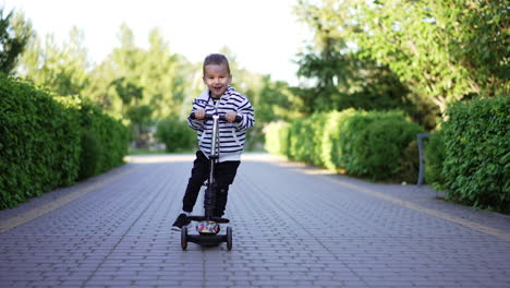 little boy learning to ride a scooter. happy kid rides a vehicle smiling adorably approaching camera.