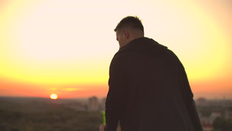 view from the back a man walks on the roof at sunset and drinks beer looking at the beautiful view of the city.